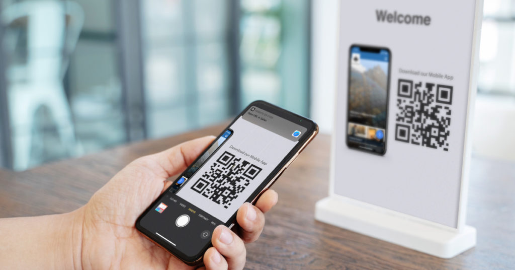 Photo of a person holding a phone, next a standee showing a QR code